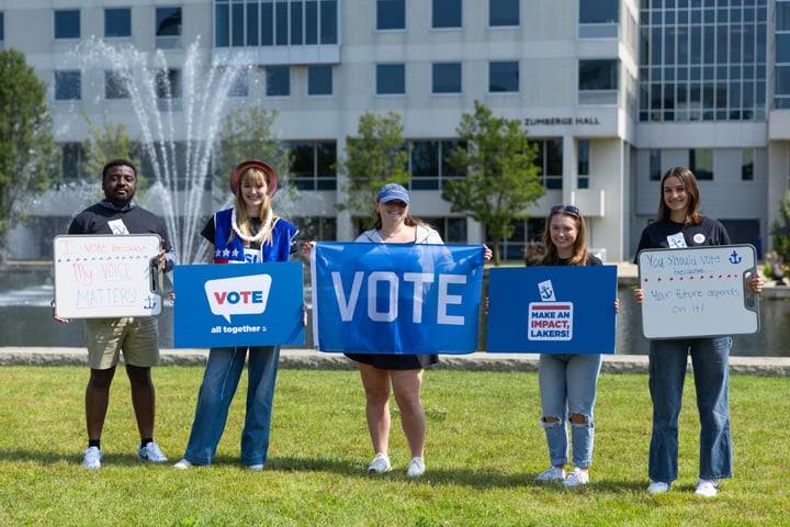 5 students holding GVSU voting signs in front of pond